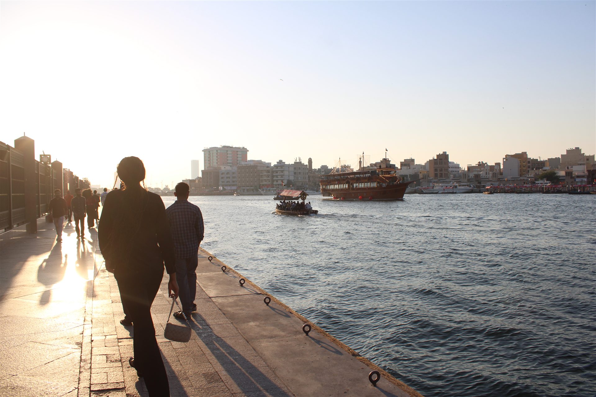 People walking beside Dubai Creek at sunset